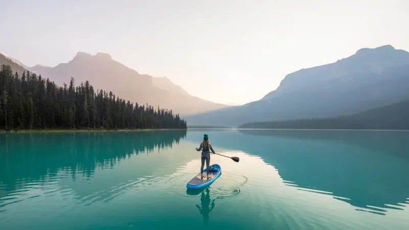 A paddleboarder on a still turquoise lake at sunrise