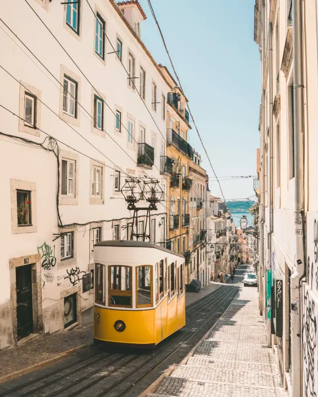 A yellow funicular climbing a narrow Lisbon street